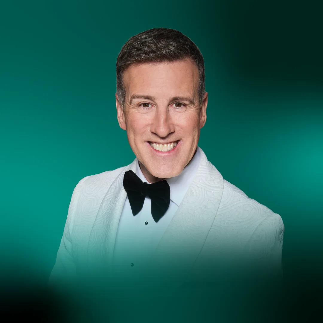 Anton Du Beke smiling in a white dinner jacket and black bow tie against a green background